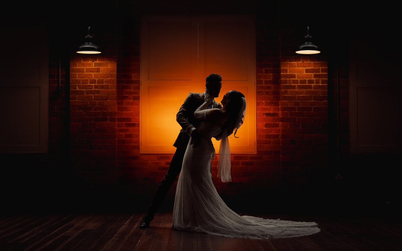Bride and groom exit a stone building, holding hands, surrounded by applauding guests and floral arrangements.