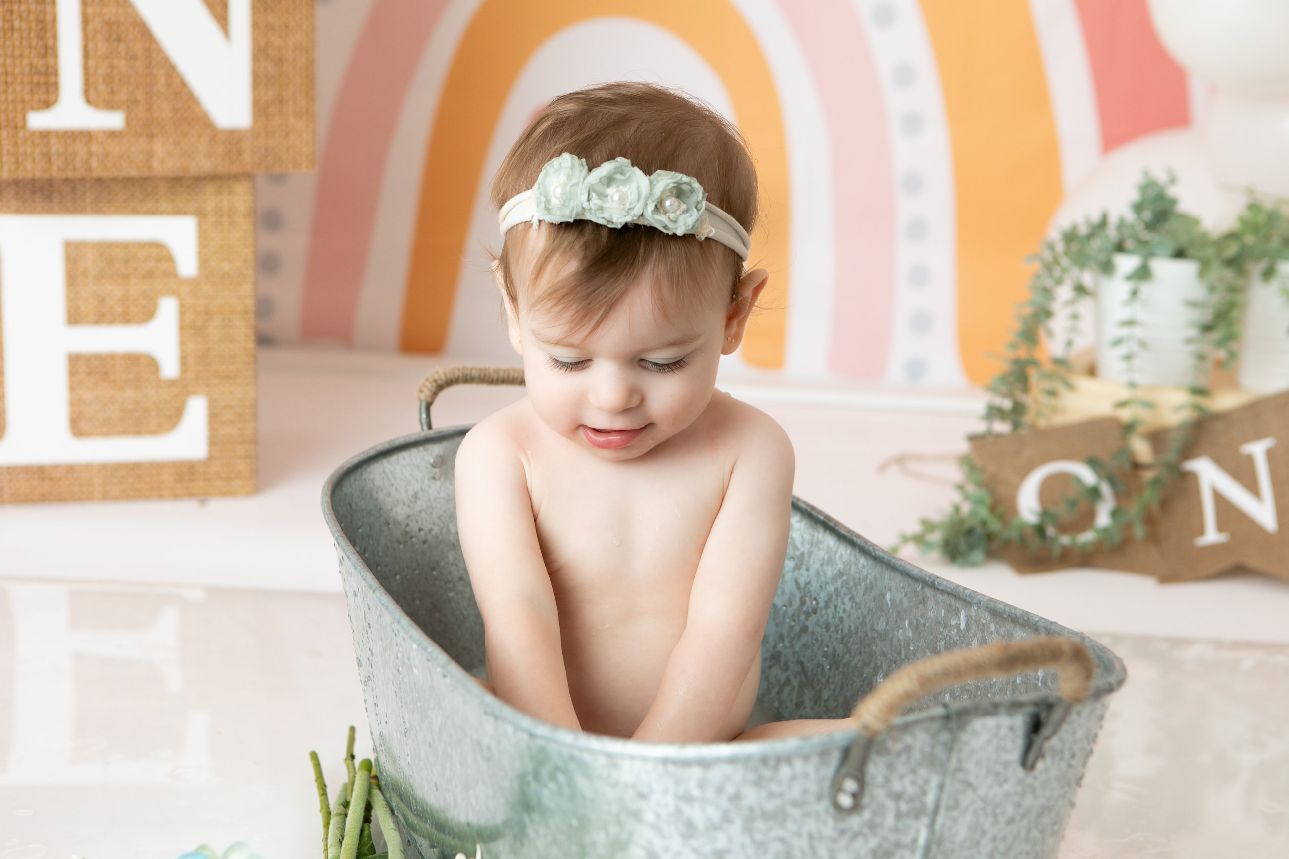 Baby with a flower headband in a tin bathtub beside a pastel rainbow