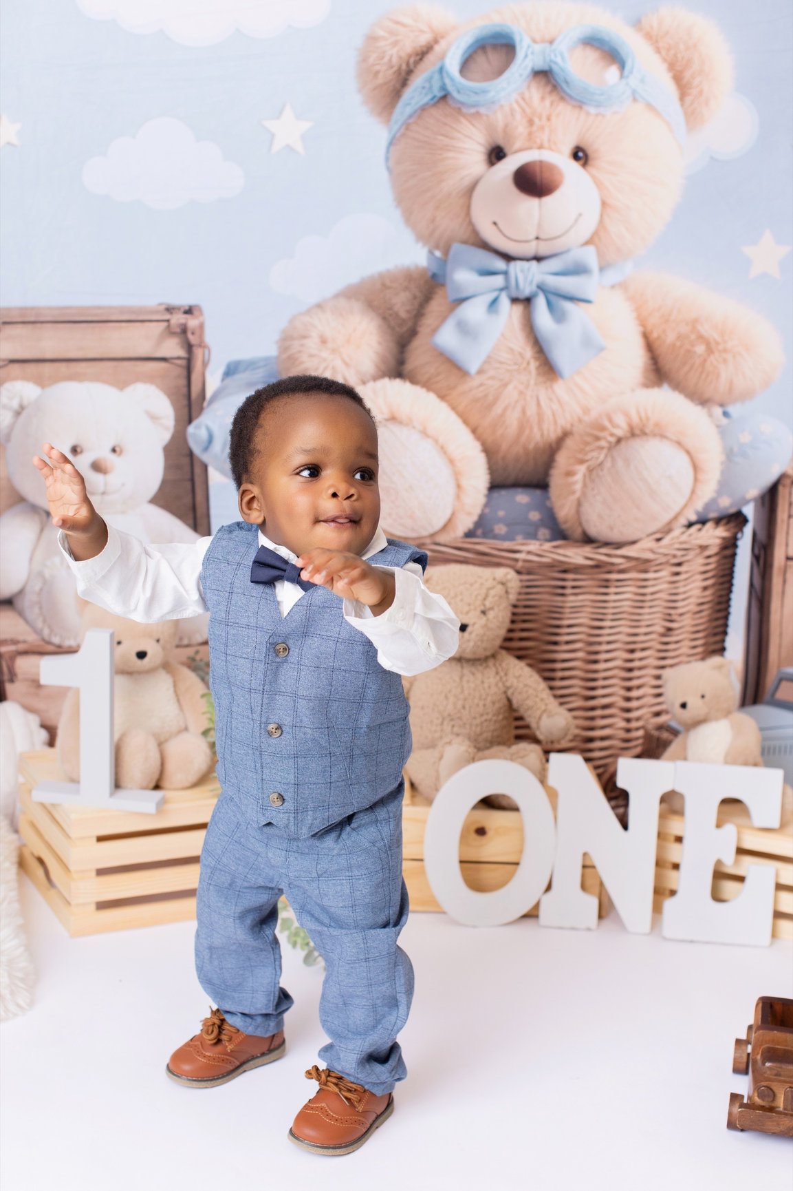 Baby in blue overalls seated with teddy bears and wooden ONE letters