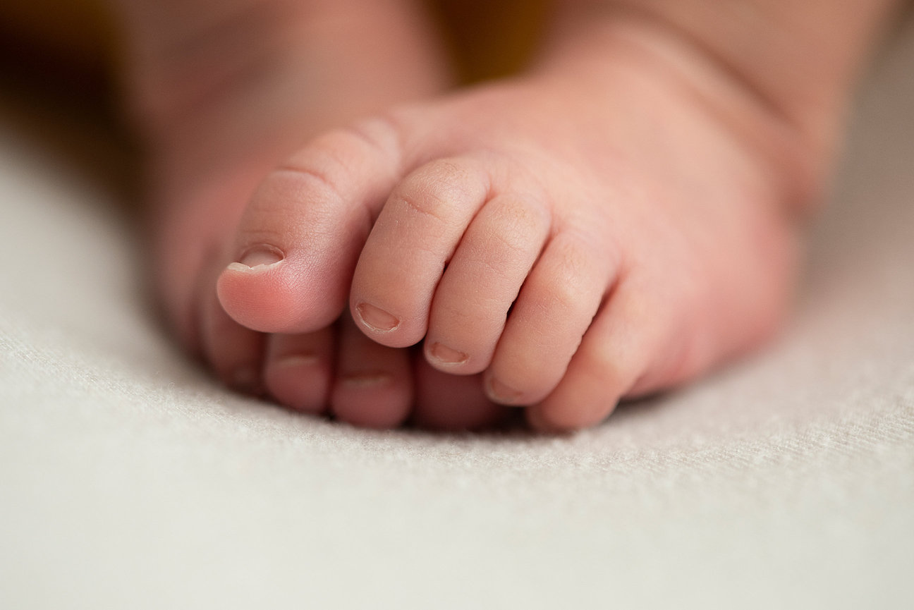 Close-up of a newborn babys feet with tiny toes gently pressed together, resting on a soft, light-colored surface. The focus is on the delicate skin texture and small nail details, evoking the warmth and innocence found in of Genoa, Illinois.
