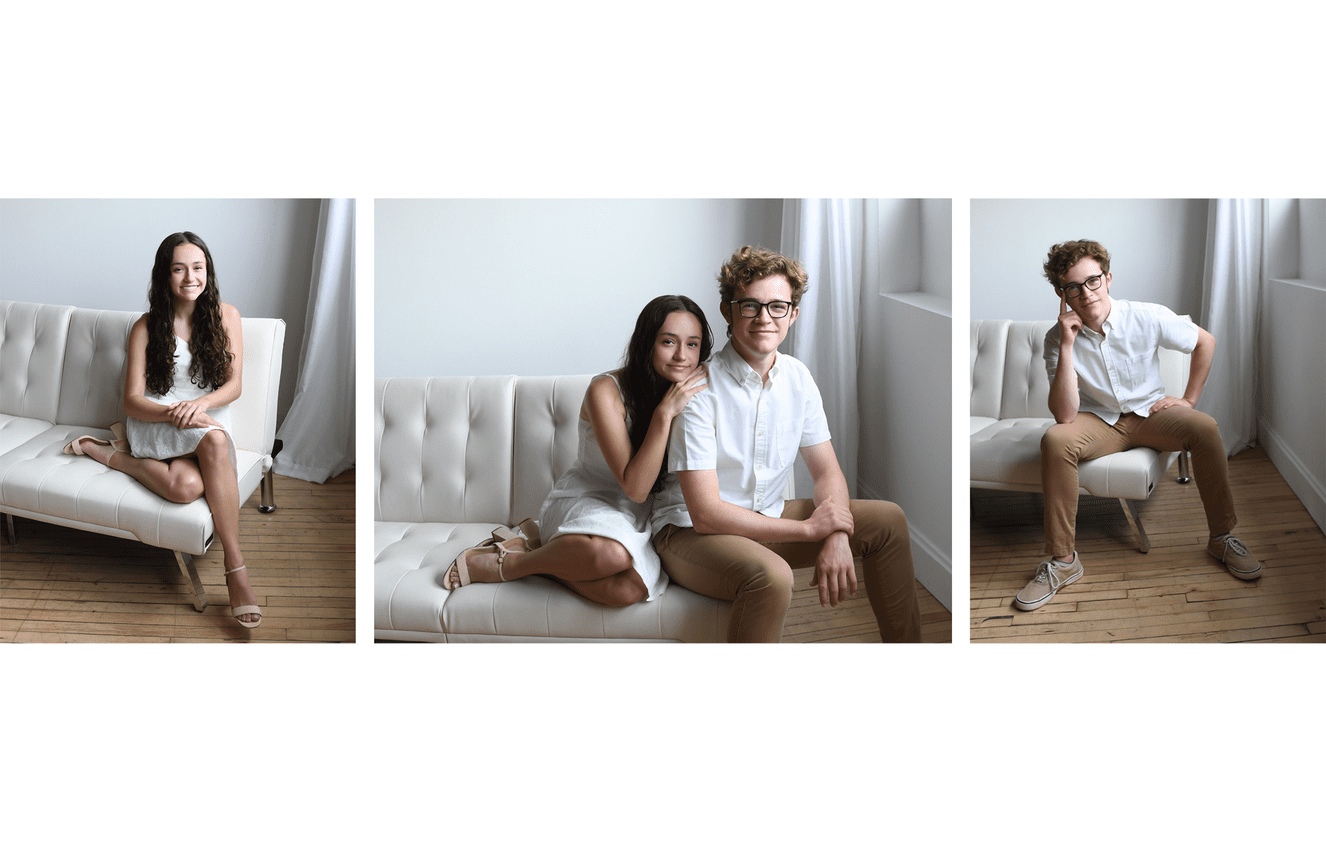 A teenage sister and her collage aged brother sit on a white couch together.