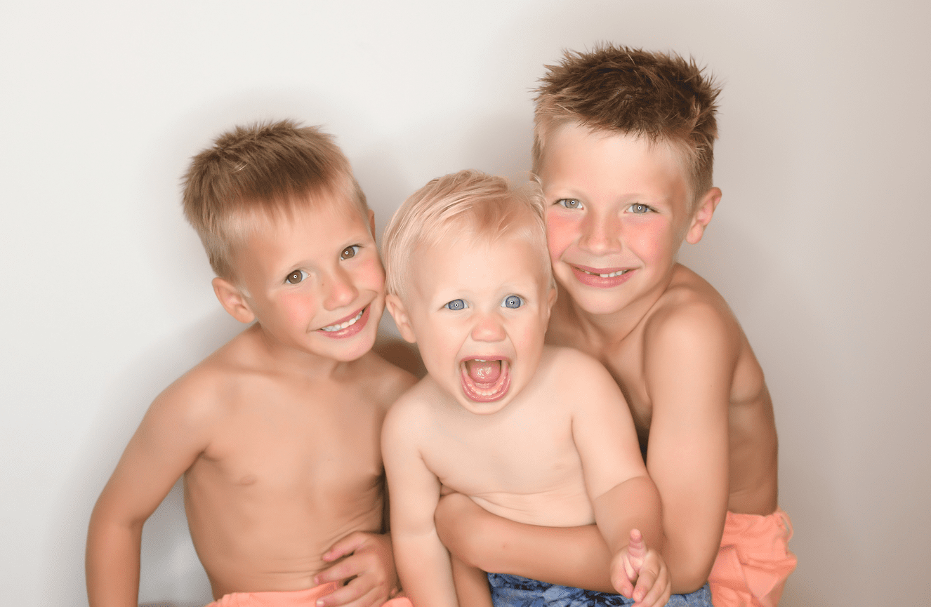 A close up of three young brothers with their arms wrapped around each other.