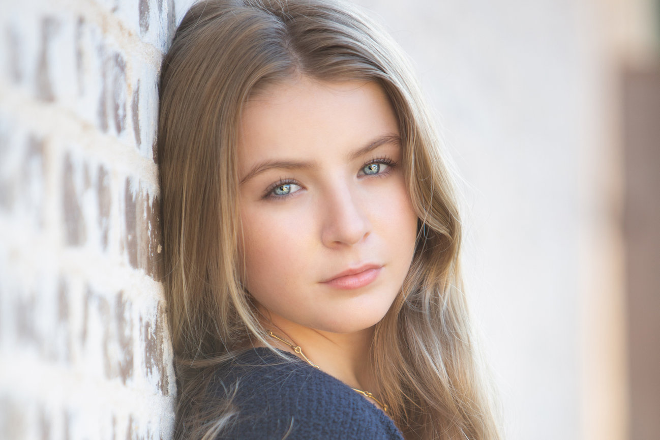 outdoor photoshoot for a headshot of a senior girl against a white brick wall