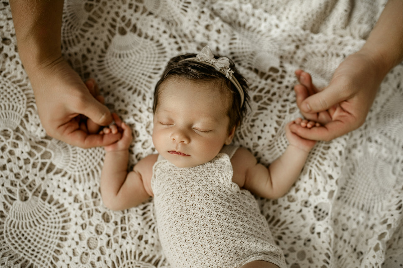 Newborn baby peacefully sleeping on a textured blanket, held gently by two adult hands.