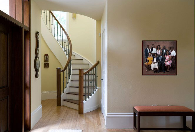 Elegant foyer with curved staircase, wooden bench, and a family portrait on the wall.