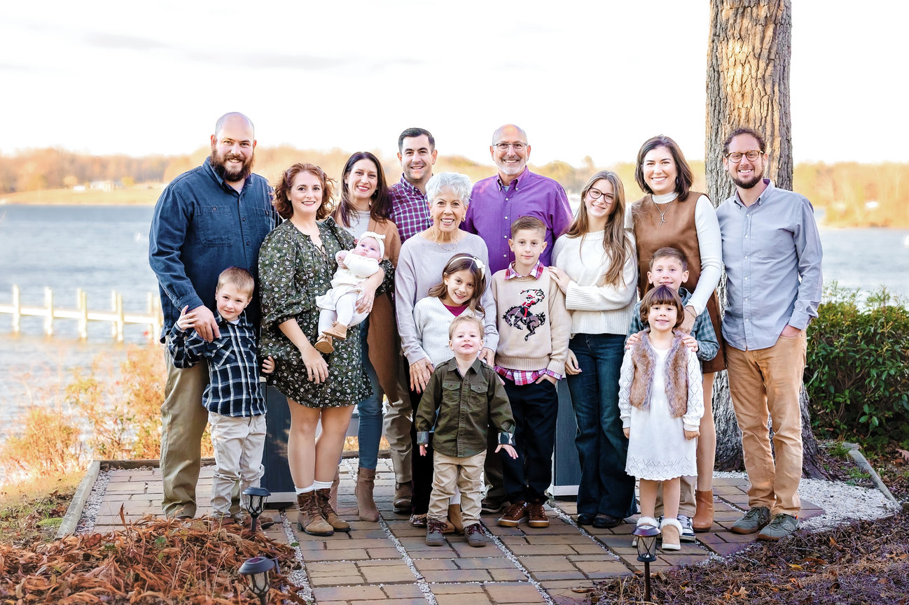 Outdoor photography session of an extended family session posing outdoors near a river, with smiles and casual clothing on a stone pathway in autumn scenery.