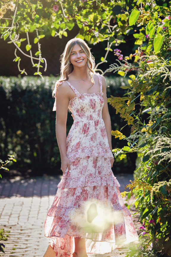 a libertyville high school senior in a floral dress standing in a sunlit garden path, surrounded by lush greenery for her senior pictures at Chicago Botanic Garden.