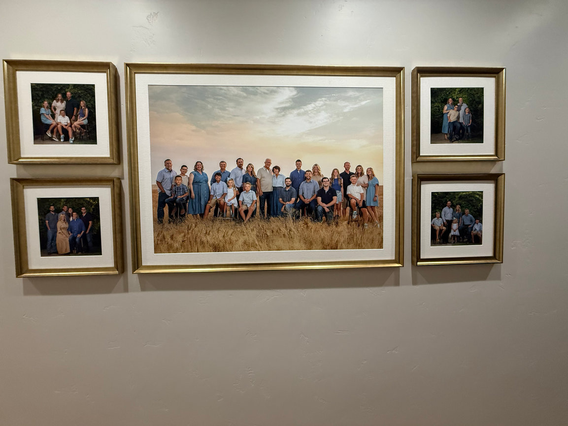 Large family portrait centered among smaller framed photos on a wall