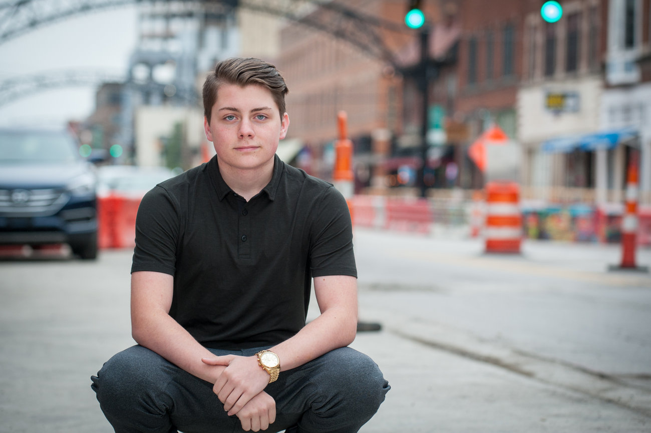 Teenage boy in a dark polo and jeans squatting on an urban street in Columbus for senior portraits.