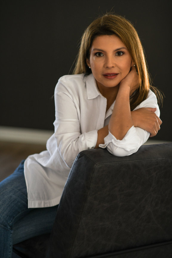 Woman in a white shirt resting her arm on a gray chair, with a soft expression against a dark background. Professional Branding and Headshots in Columbus Ohio.