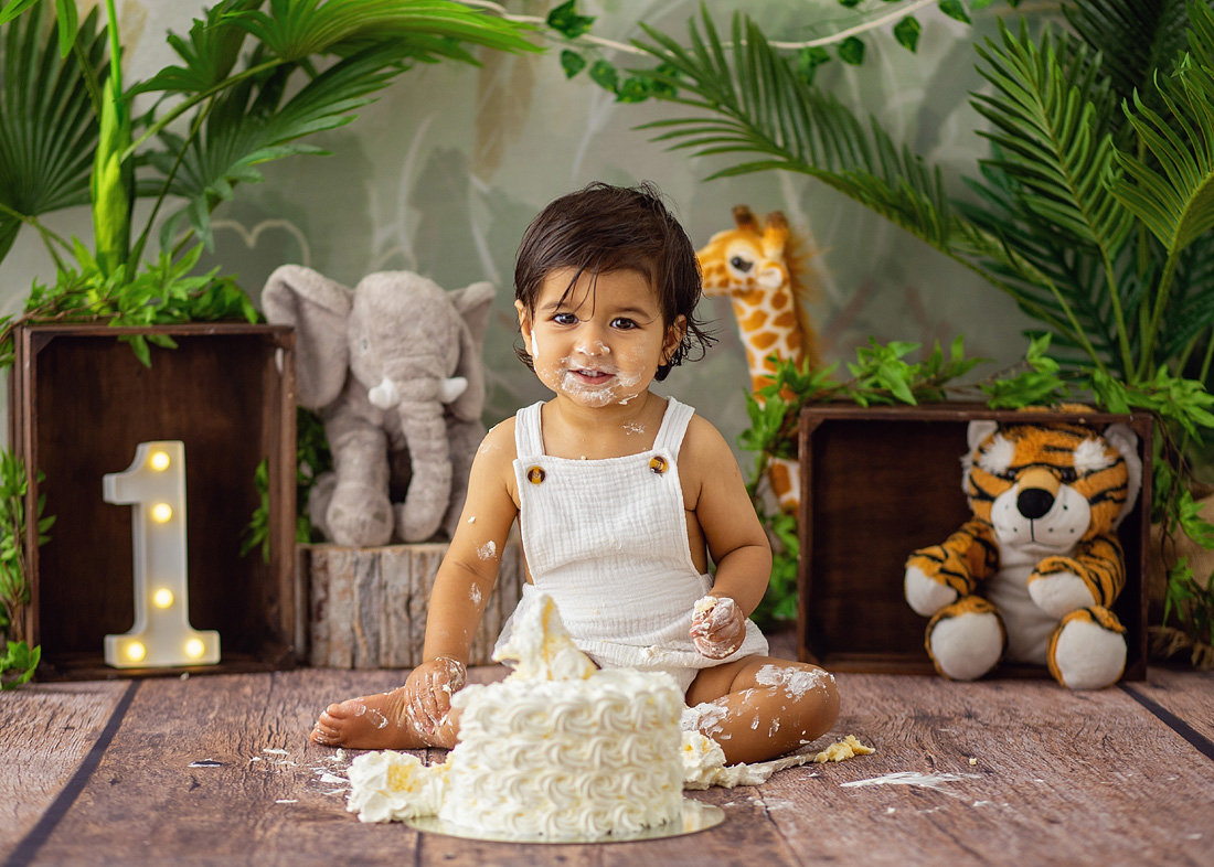 Smiling baby sitting in front of a white rosette cake during a safari-themed cake smash with jungle animals and greenery by Cake Smash by Chris in Point Cook.