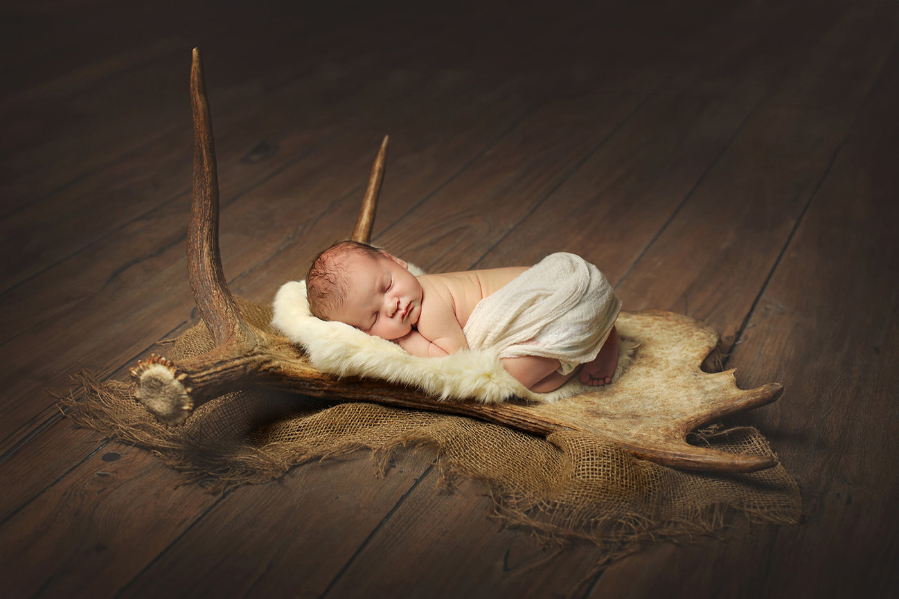 Baby sleeping on soft fabric atop antlers, on a wooden floor background.
