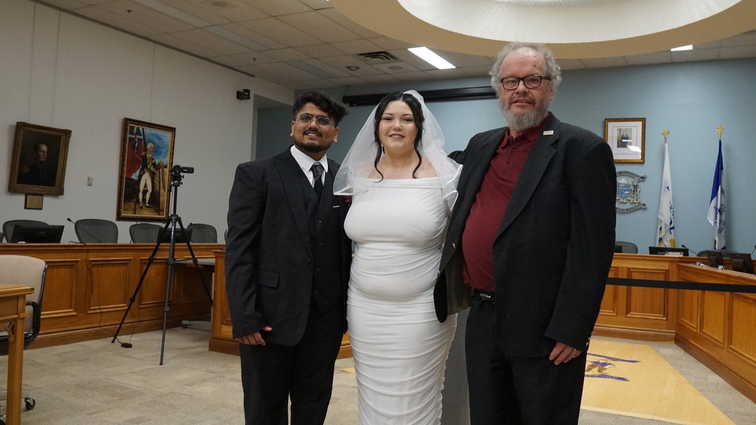 Bride and groom posing with family member in a ceremony room