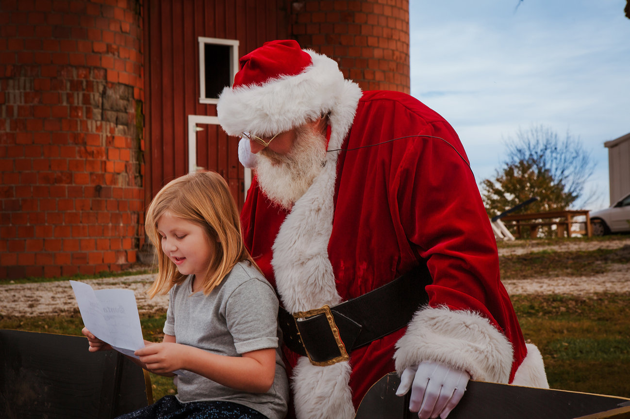 A young girl reads a letter beside Santa during an earlier holiday visit